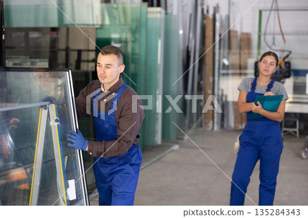 Worker moving insulated glass units on rack across factory floor Worker moving insulated glass units on rack across factory floor 135284343