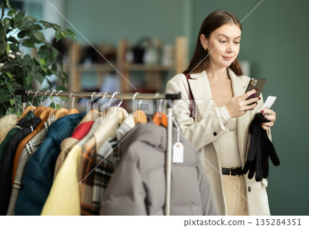 Young woman scanning QR-code on gloves in clothing store 135284351