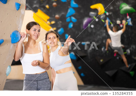 Young women are standing in gym and discussing possible options for overcoming difficult climbing route 135284355