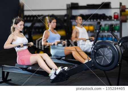 Athletic woman in sportswear training on rowing machine in sport gym Athletic woman in sportswear training on rowing machine in sport gym 135284405