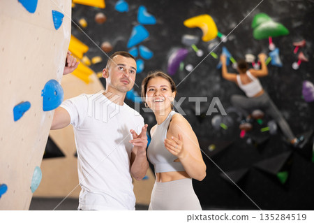 Girl gym coach and teen client standing in fitness room discussing possible options climbing Girl gym coach and teen client standing in fitness room discussing possible options climbing 135284519