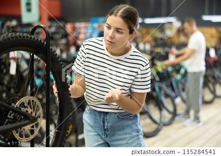 Young buyer female checking tire on wheel in bicycle store Young buyer female checking tire on wheel in bicycle store 135284541