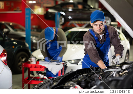 Young guy mechanic repairs under hood of car Young guy mechanic repairs under hood of car 135284548