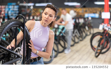 Female cyclist carefully examining bike wheel in store 135284552
