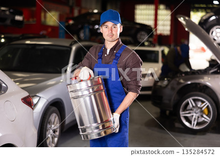 Positive male worker of car workshop holding metal fuel canister 135284572