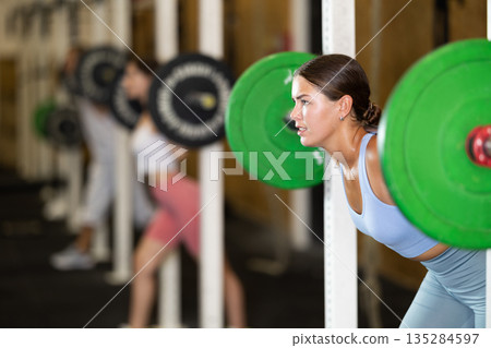 Young woman lifting barbell in gym Young woman lifting barbell in gym 135284597