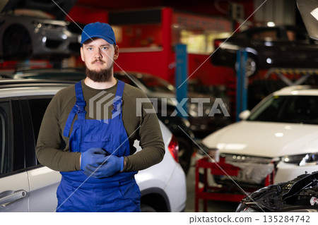 Portrait of professional auto mechanic in uniform near car on lift in car service center 135284742