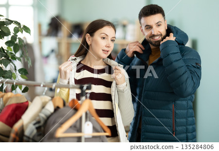 Woman choose coat in clothing store. Man try on down jacket 135284806