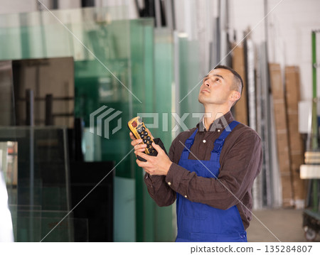Male worker using control panel and lifting mechanism controls movement of window panes in an industrial workshop 135284807
