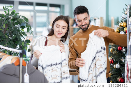 European happy couple buyers standing in clothing market and carefully examines selection of sweaters on sale of winter clothing collection European happy couple buyers standing in clothing market and carefully examines selection of sweaters on sale of winter clothing collection 135284811