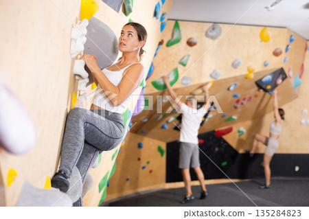 Young woman climbs steep artificial wall in sports complex and trains endurance Young woman climbs steep artificial wall in sports complex and trains endurance 135284823
