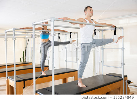 Girl and man is stretching body with pilates machine Girl and man is stretching body with pilates machine 135284849
