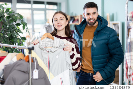 Man try on down jacket, woman elect coat or jacket. Family mutual shopping time Man try on down jacket, woman elect coat or jacket. Family mutual shopping time 135284879