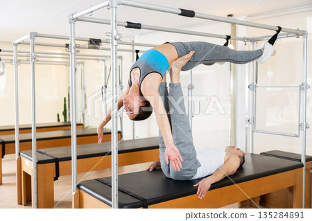 Couple practicing acroyoga on Pilates trapeze table in studio Couple practicing acroyoga on Pilates trapeze table in studio 135284891