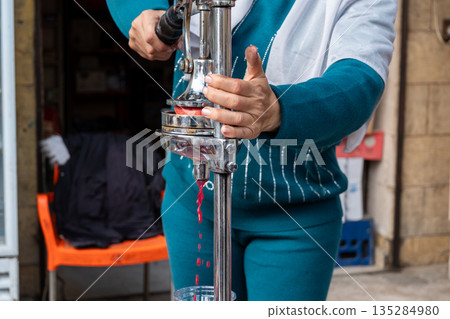 A woman extracts pomegranate juice using a manual juicer. She has dark hair and wears a blue outfit. The scene is set in a market environment. 135284980