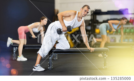 Athletic man pumping her biceps with a dumbbell while leaning on bench Athletic man pumping her biceps with a dumbbell while leaning on bench 135285000