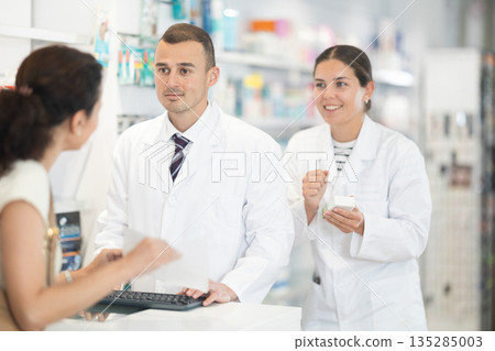 Male and female pharmacists speaking to woman customer buying medical preparation in drugstore Male and female pharmacists speaking to woman customer buying medical preparation in drugstore 135285003