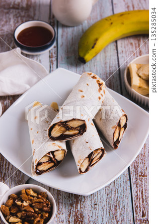 Chocolate covered banana slices wrapped in a tortilla on a plate on a table vertical view 135285034