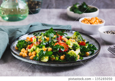 Vegetarian salad with chickpeas, tomatoes, broccoli and greens on a plate on the table 135285050