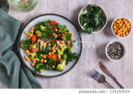 Vegetarian salad with chickpeas, tomatoes, broccoli and greens on a plate on the table top view 135285054