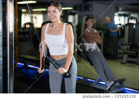 Athletic girl work out muscles of arms and shoulders on rope loop simulator in gym of fitness club 135285138