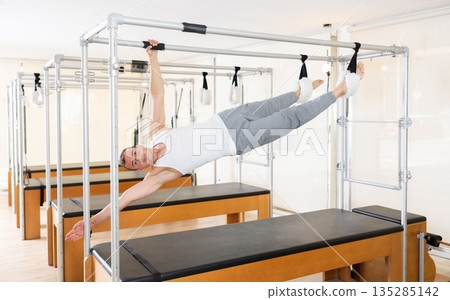 Man does pilates suspended on special sports equipment Man does pilates suspended on special sports equipment 135285142