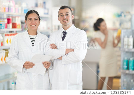 Young male and female pharmacists posing in pharmacy Young male and female pharmacists posing in pharmacy 135285174