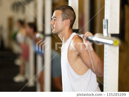 Man in activewear exercising with barbell during group workout in gym center Man in activewear exercising with barbell during group workout in gym center 135285209