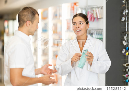 Girl pharmacist offers male client transparent blue bottle Girl pharmacist offers male client transparent blue bottle 135285242