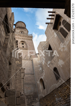 Historic Qalawun Complex in Cairo, featuring intricate architecture, tall minarets, and domes under a blue sky with clouds. A significant cultural landmark on Al-Muizz Street. Historic Qalawun Complex in Cairo, featuring intricate architecture, tall minarets, and domes under a blue sky with clouds. A significant cultural landmark on Al-Muizz Street. 135285370