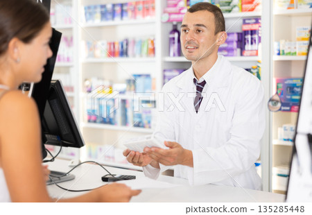 Male pharmacist consulting young girl about medicament in box Male pharmacist consulting young girl about medicament in box 135285448