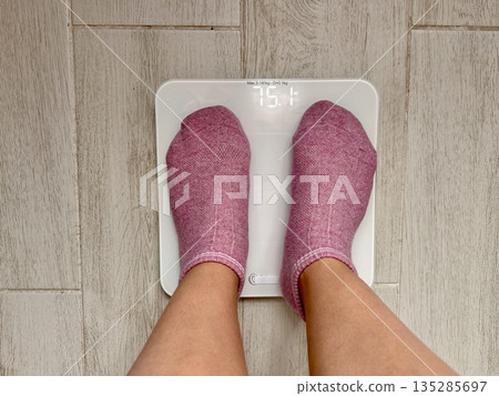 A young girl stands on an electronic floor scale to measure excess weight at home 135285697