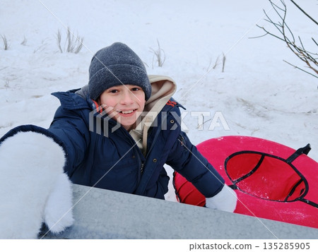 Happy young boy outdoors with a red tubing on a snow slide 135285905