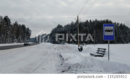Bus stop in the middle of a beautiful winter road in the middle of the forest with a bus stop sign. A bus stop in the middle of a forest outside the city in winter Bus stop in the middle of a beautiful winter road in the middle of the forest with a bus stop sign. A bus stop in the middle of a forest outside the city in winter 135285911