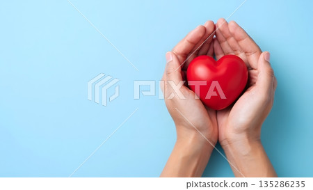 Caring Hands Holding a Bright Red Heart on a Soft Blue Background Caring Hands Holding a Bright Red Heart on a Soft Blue Background 135286235