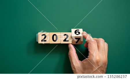 Hand Changing Year on Wooden Blocks from 2026 to 2027 on Green Background Hand Changing Year on Wooden Blocks from 2026 to 2027 on Green Background 135286237