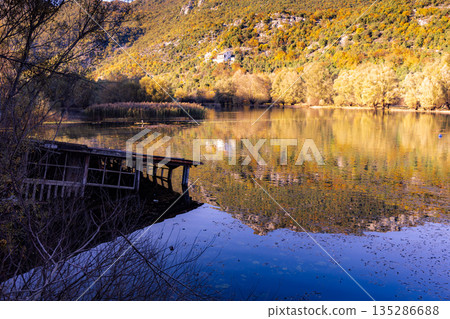 Autumn Lake Scene With Reflections, Mountains, And A Weathered Dock By Calm Water Autumn Lake Scene With Reflections, Mountains, And A Weathered Dock By Calm Water 135286688