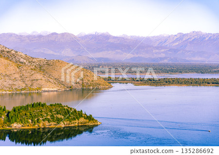 Tranquil Lake Amid Mountain Range With Islands and Hills Under Clear Sky 135286692