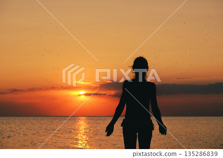 Silhouette of the woman standing lonely at the sea during beautiful sunset. Download image 135286839