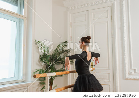 Young ballerina in tutu skirt stretching practicing ballet positions dancing near ballet barre in dance class. Young classical dancer woman in dance studio. Ballet class training Ballet school concept 135287950