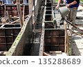 Construction workers pour concrete into molds at a building site during daylight hours in a developing urban area 135288689