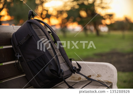 Backpack Resting on Park Bench at Sunset in Warm Golden Light Backpack Resting on Park Bench at Sunset in Warm Golden Light 135288926