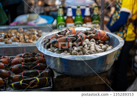 Live crabs stacked on a tray at a Thai street food stall, their claws tied as they wait for sale, capturing the raw and authentic atmosphere of local market life. Live crabs stacked on a tray at a Thai street food stall, their claws tied as they wait for sale, capturing the raw and authentic atmosphere of local market life. 135289353