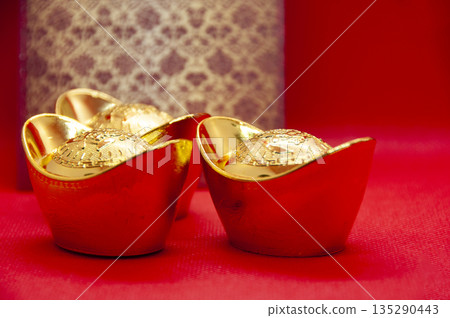 Golden ingots centered on red surface with soft lighting for Chinese New Year wealth symbolism. Golden ingots centered on red surface with soft lighting for Chinese New Year wealth symbolism. 135290443
