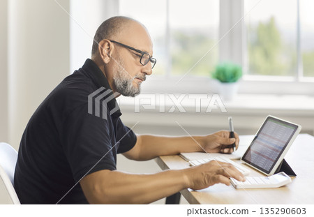 Mature man working with spreadsheet on tablet and calculator at home office Mature man working with spreadsheet on tablet and calculator at home office 135290603