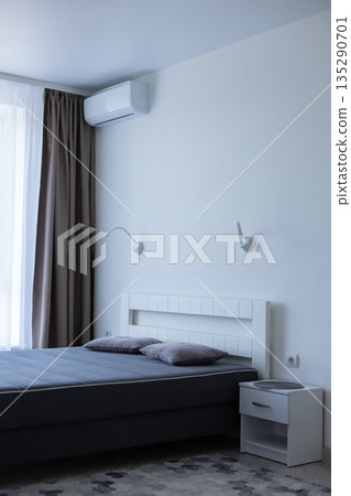 Light bedroom with bed near window and air conditioner above the bed. Bedroom interior. 135290701