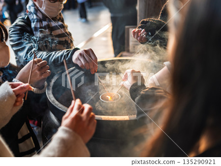 Close focus on tourists' hands burning the small incenses with smoke inside the big pot. Close focus on tourists' hands burning the small incenses with smoke inside the big pot. 135290921