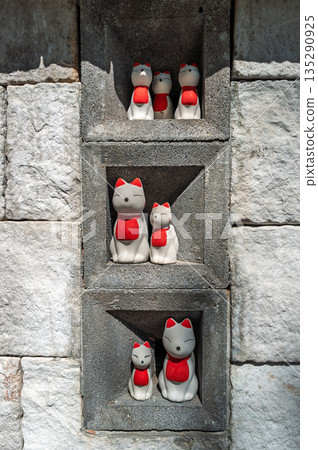 The fox dolls in white and red color decorated in the holes of grey stone wall. 135290925