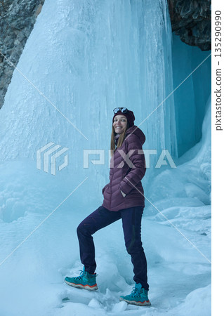 Woman tourist exploring a frozen waterfall, natural ice formation. Winter travel Woman tourist exploring a frozen waterfall, natural ice formation. Winter travel 135290990