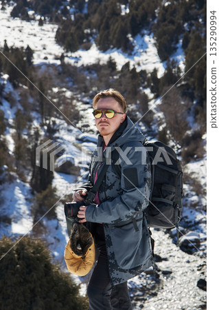 Young man hiker with backpack and camera on a winter mountain adventure Young man hiker with backpack and camera on a winter mountain adventure 135290994